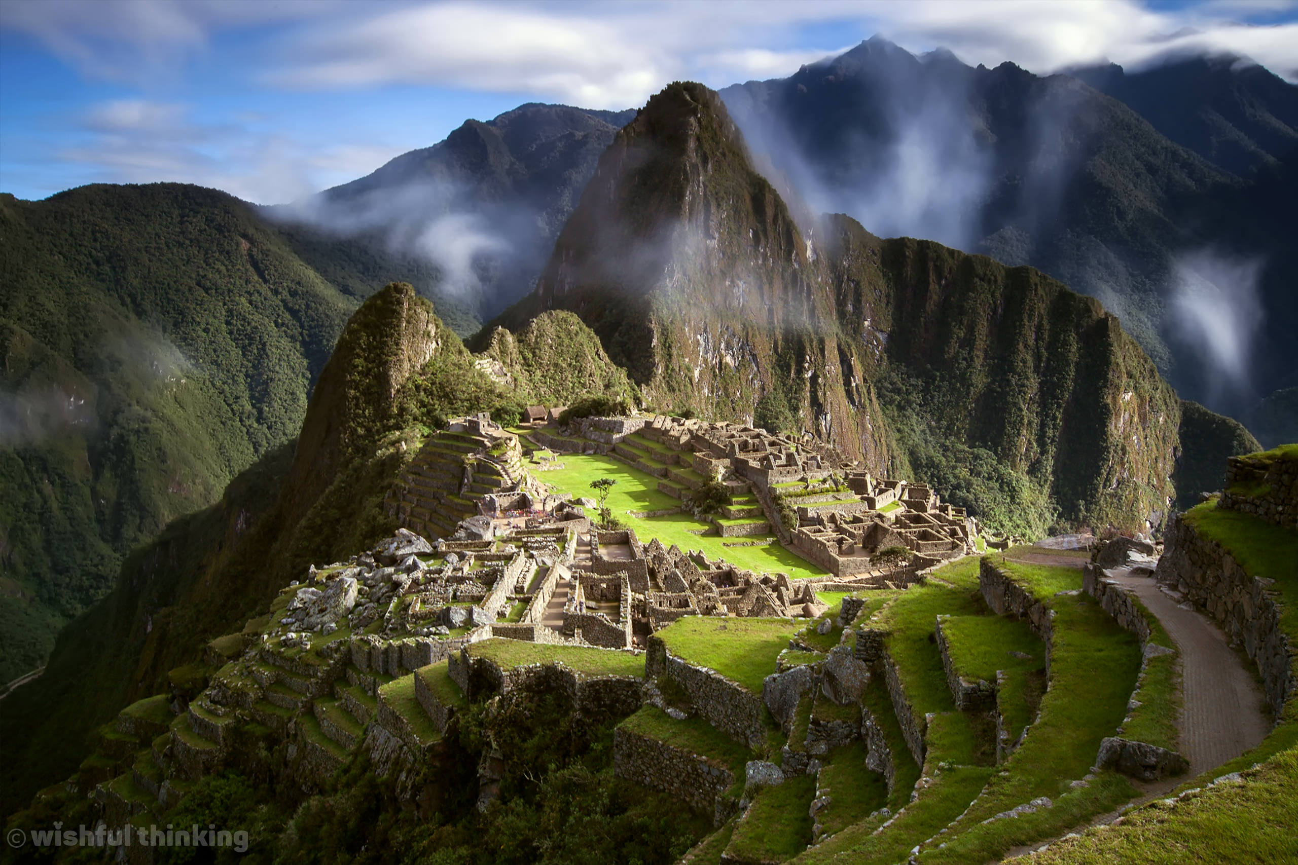 Wisps of misty clouds float above the peaks of Macchu Picchu in the mountains of Peru