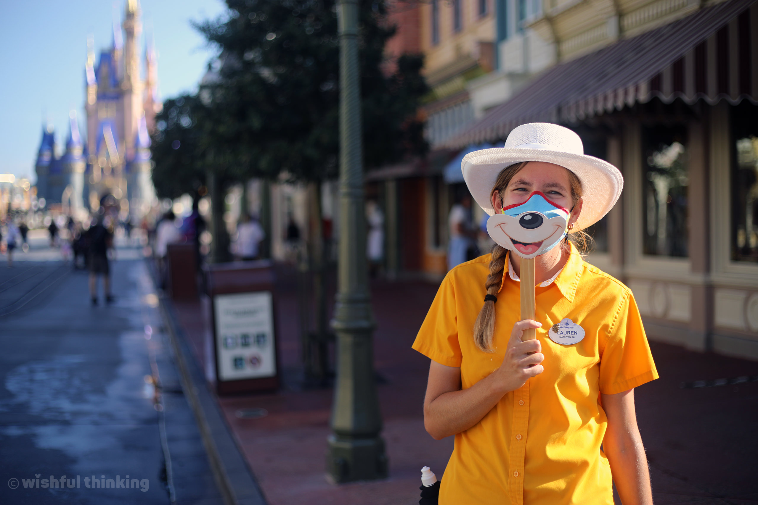 A smiling Walt Disney World Cast Member demonstrates how to wear a facial covering for COVID-19 Protections