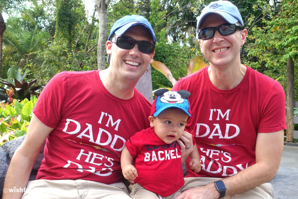 At Magic Kingdom, two dads in red t-shirts smile with their son at Gay Days in Walt Disney World, Orlando, Florida