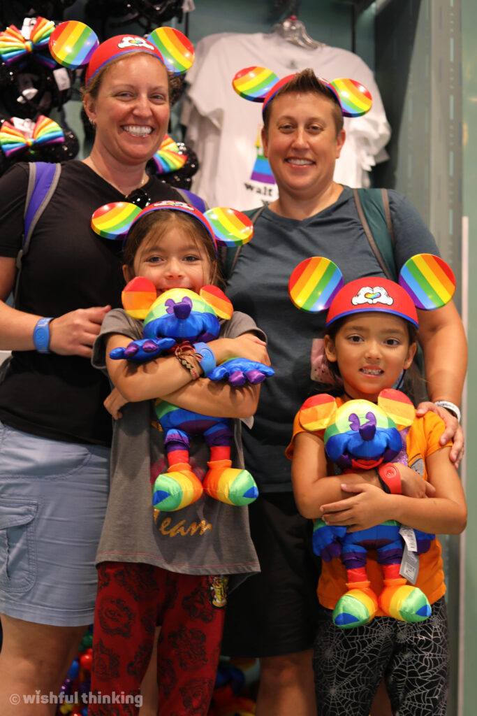 During Gay Days weekend a family with two moms hug their young kids, wearing rainbow Mickey Mouse ears and celebrating LGBTQ+ pride