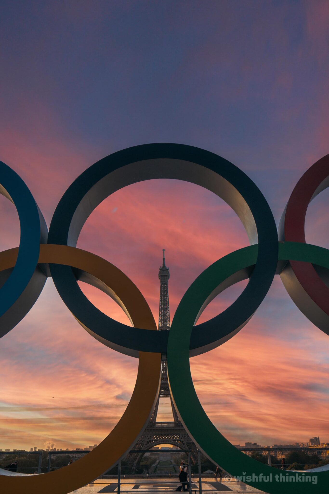During a pink-hued sunset, the Paris 2024 Olympic Rings frame the silhouette of the Eiffel Tower as Paris prepares for the Olympic and Paralympic Games