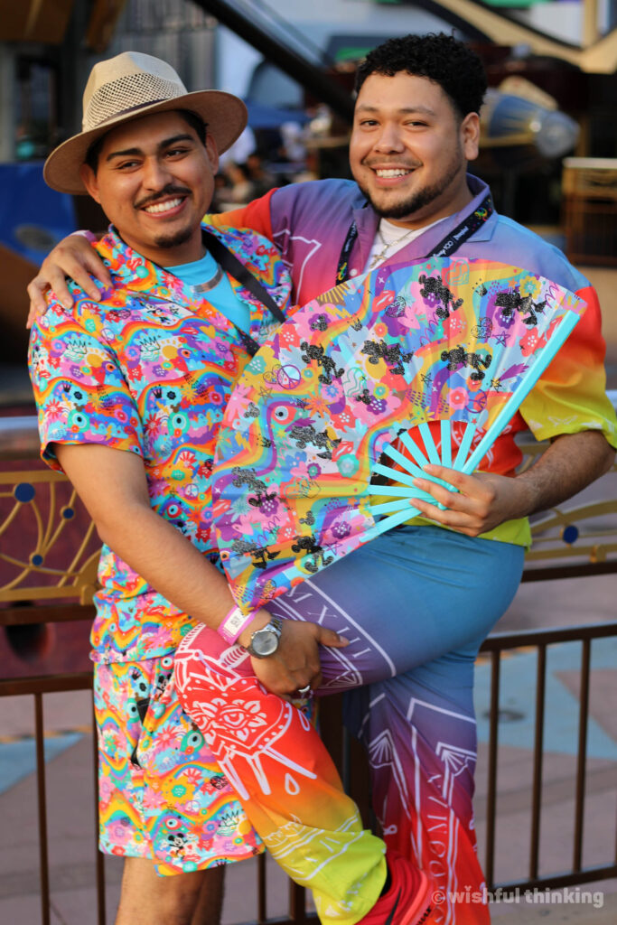 A latino gay couple show off their DIsneyland After Dark Pride Nite merchandise in Tomorrowland at Disneyland Park in 2023