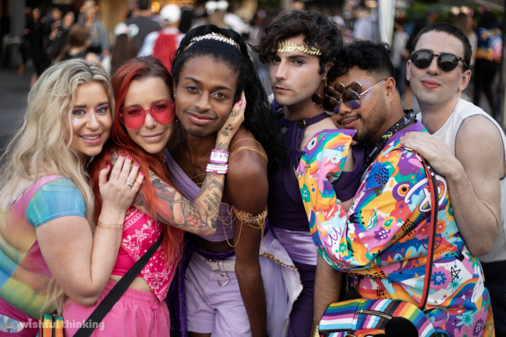 A group of young adult friends embraces tightly during Disneyland After Dark Pride Nite in June, 2023 at the Disneyland Resort in California