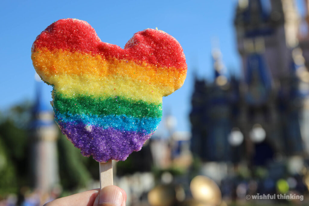 A Mickey-shaped krispie rice treat with rainbow sugar, held aloft on a sunny day at Magic Kingdom Park in Walt Disney World