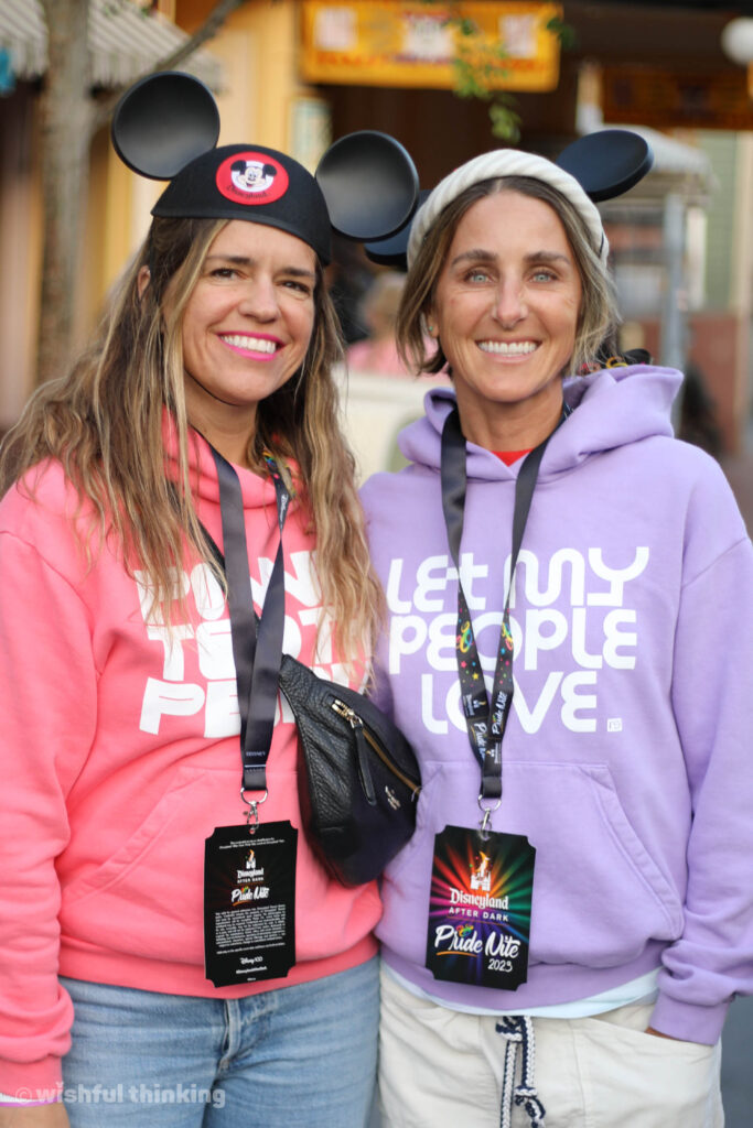 A lesbian couple in pastel sweatshirts hugs and smiles during the Disneyland After Dark Pride Nite party in 2023 in southern California